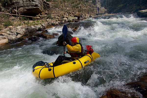 One paddler in a pack raft, heading through low grade rapids