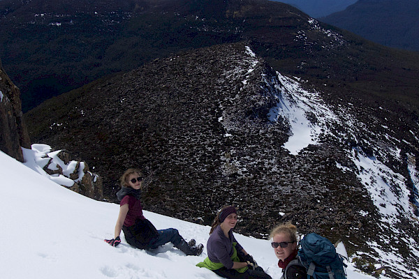 Three walkers sitting in the snow on the slopes of Mt Ossa