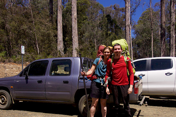 Two people standing in front of a ute, wearing big backpacks