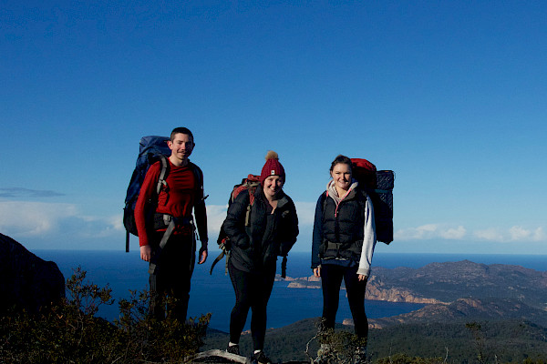 Three people standing on a peak with water in the background