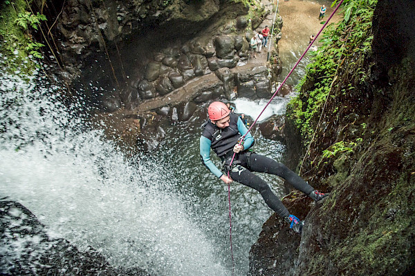 Person abseiling down a rock face with a waterfall nearby